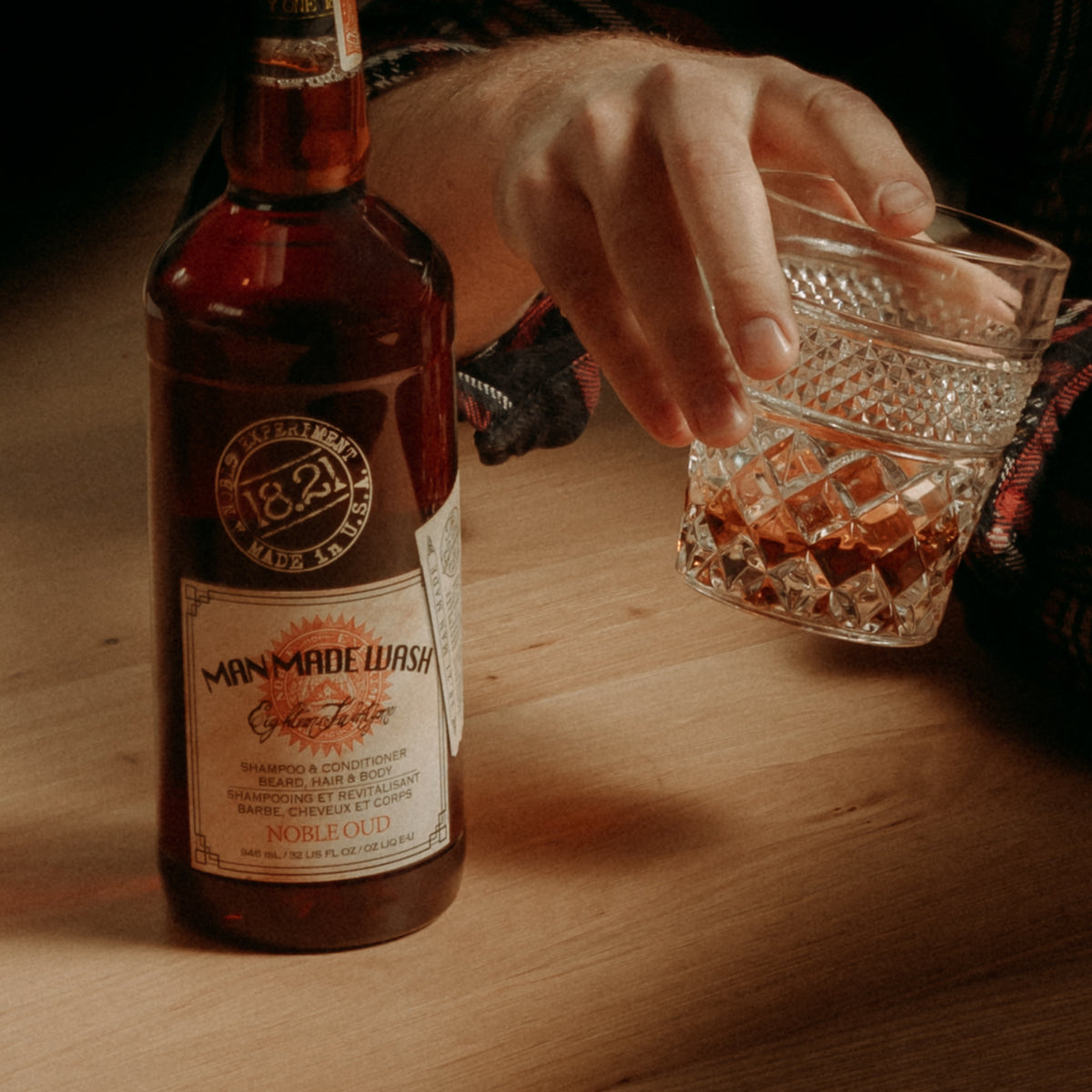 Man made Wash bottle with a hand holding a glass of whiskey on a wooden surface
