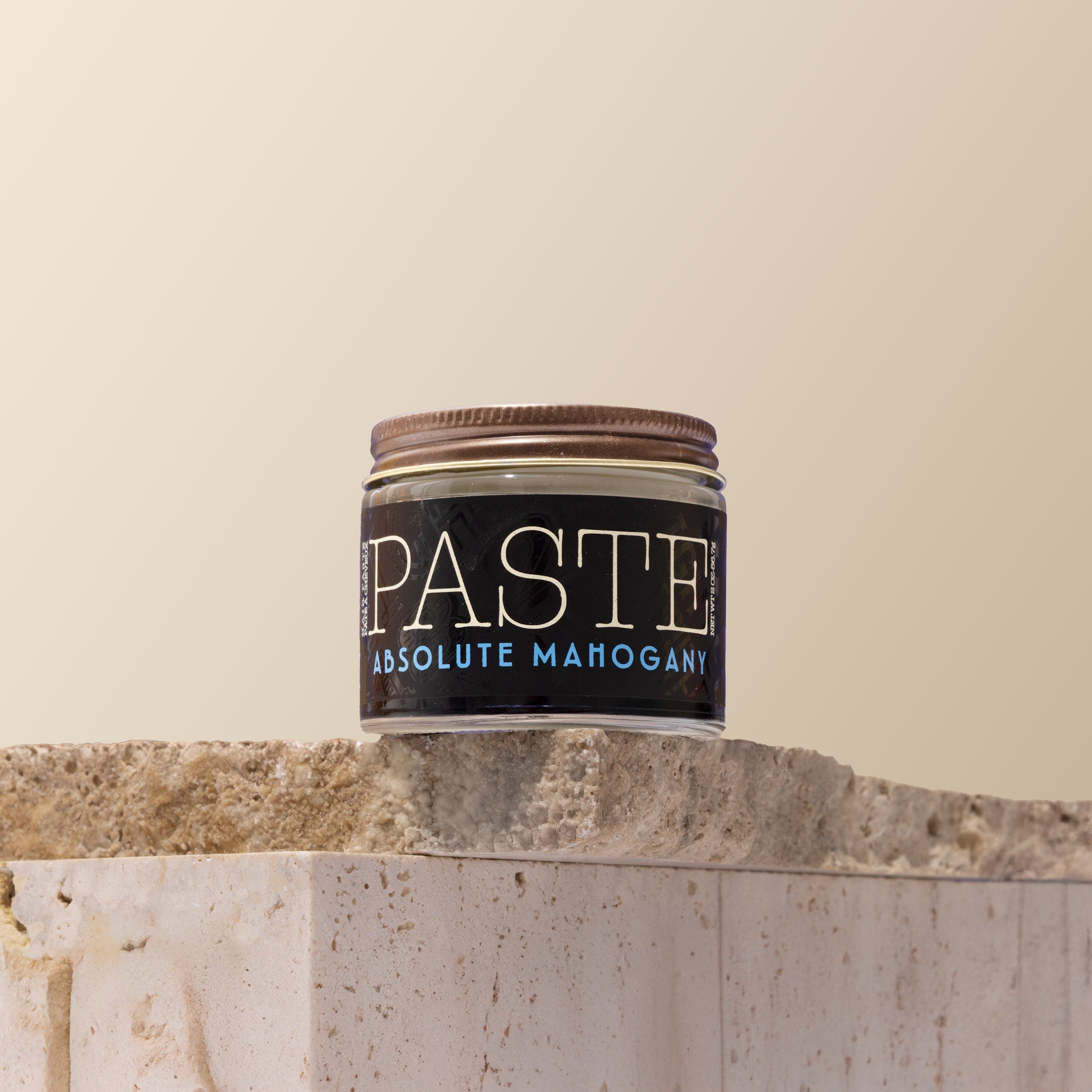 Jar of 'Paste' Absolute Mahogany hair product on a stone surface with a beige background