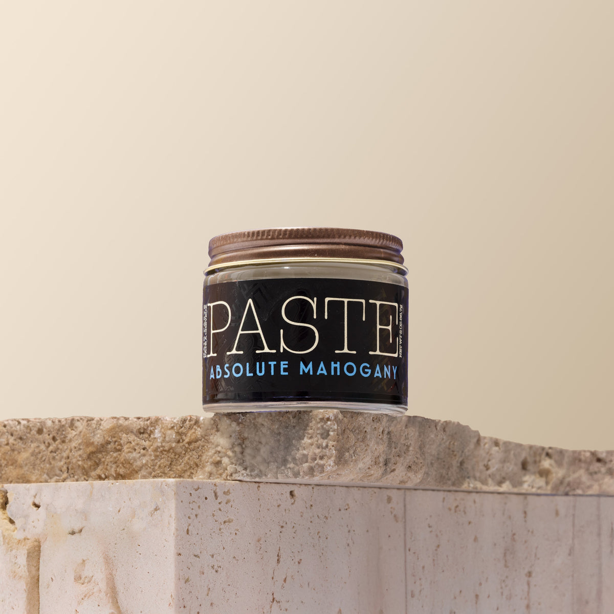 Jar of 'Paste' Absolute Mahogany hair product on a stone surface with a beige background