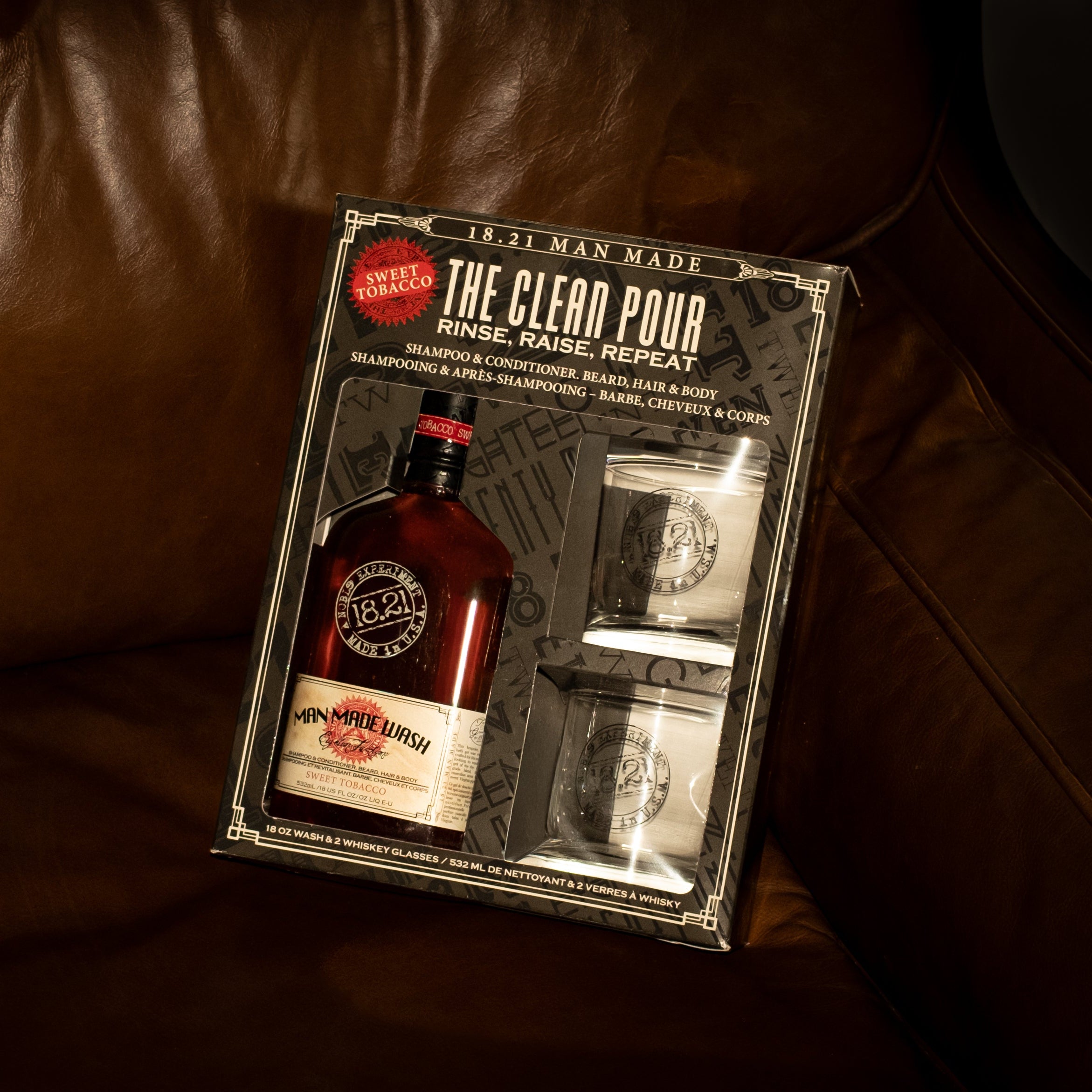 Bottle of 18.21 Man Made Wash with 2 whiskey rocks glasses in gift set on leather couch