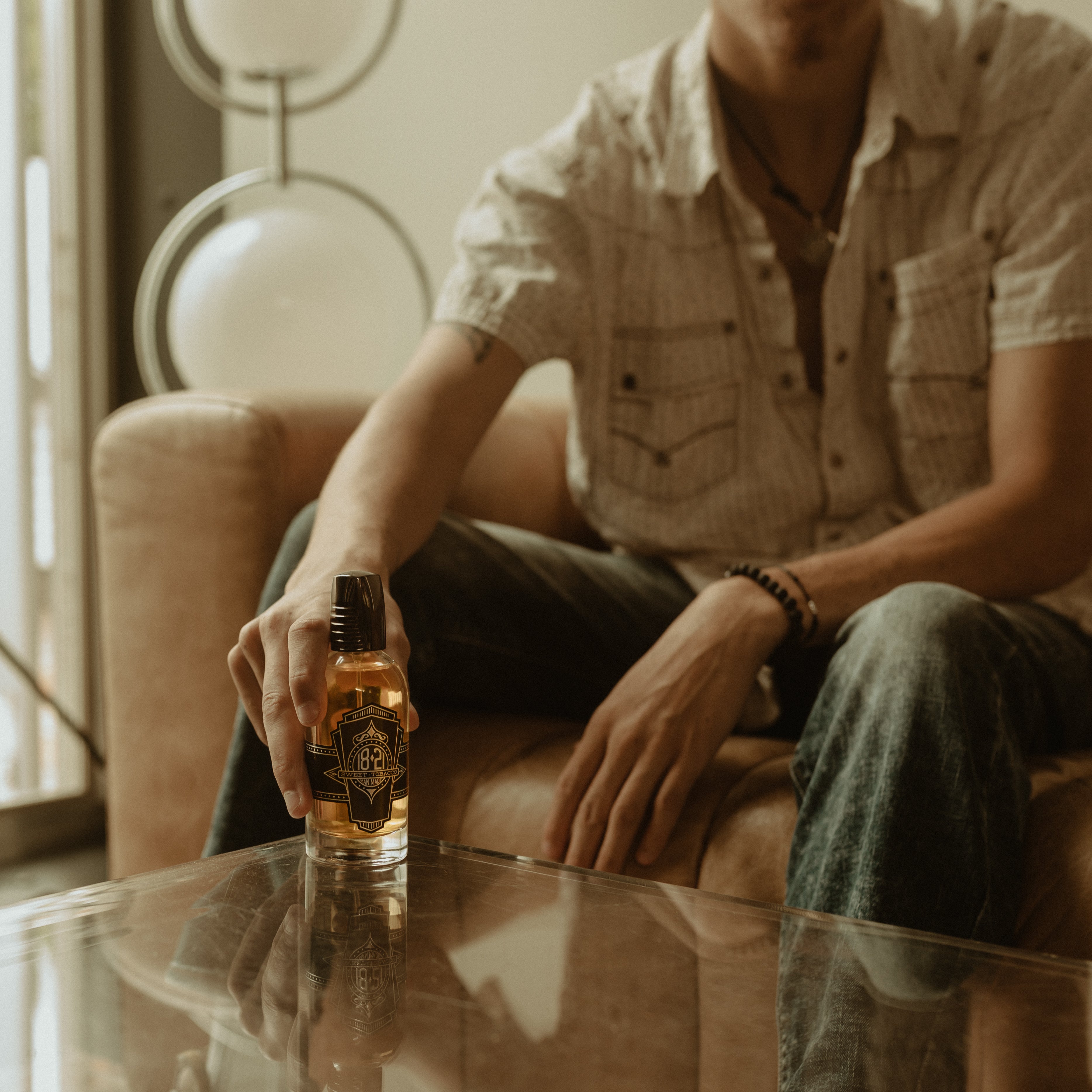 Man sitting on a couch holding a bottle of 18.21 Man Made cologne