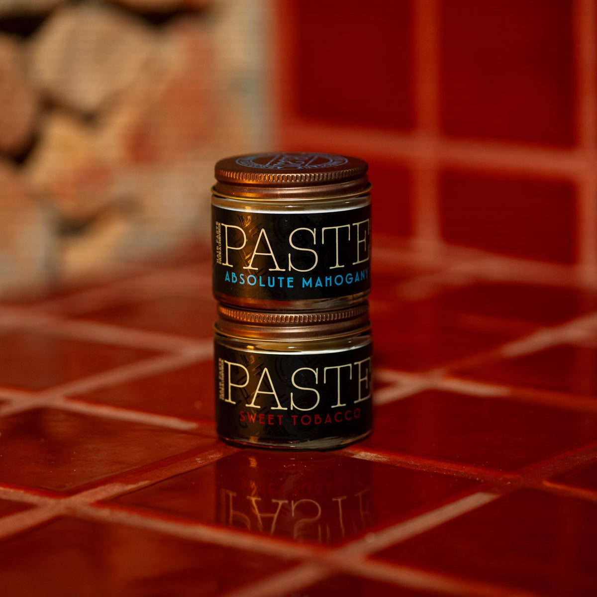Absolute Mahogany and Sweet Tobacco Styling Paste stacked upon each other on red tile