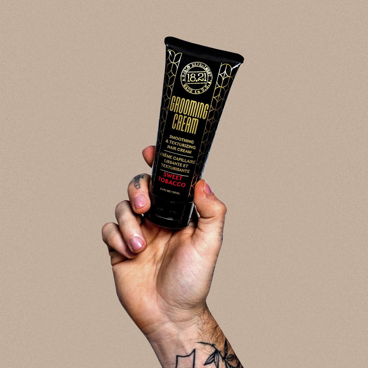 Hand holding a tube of grooming cream against a beige background