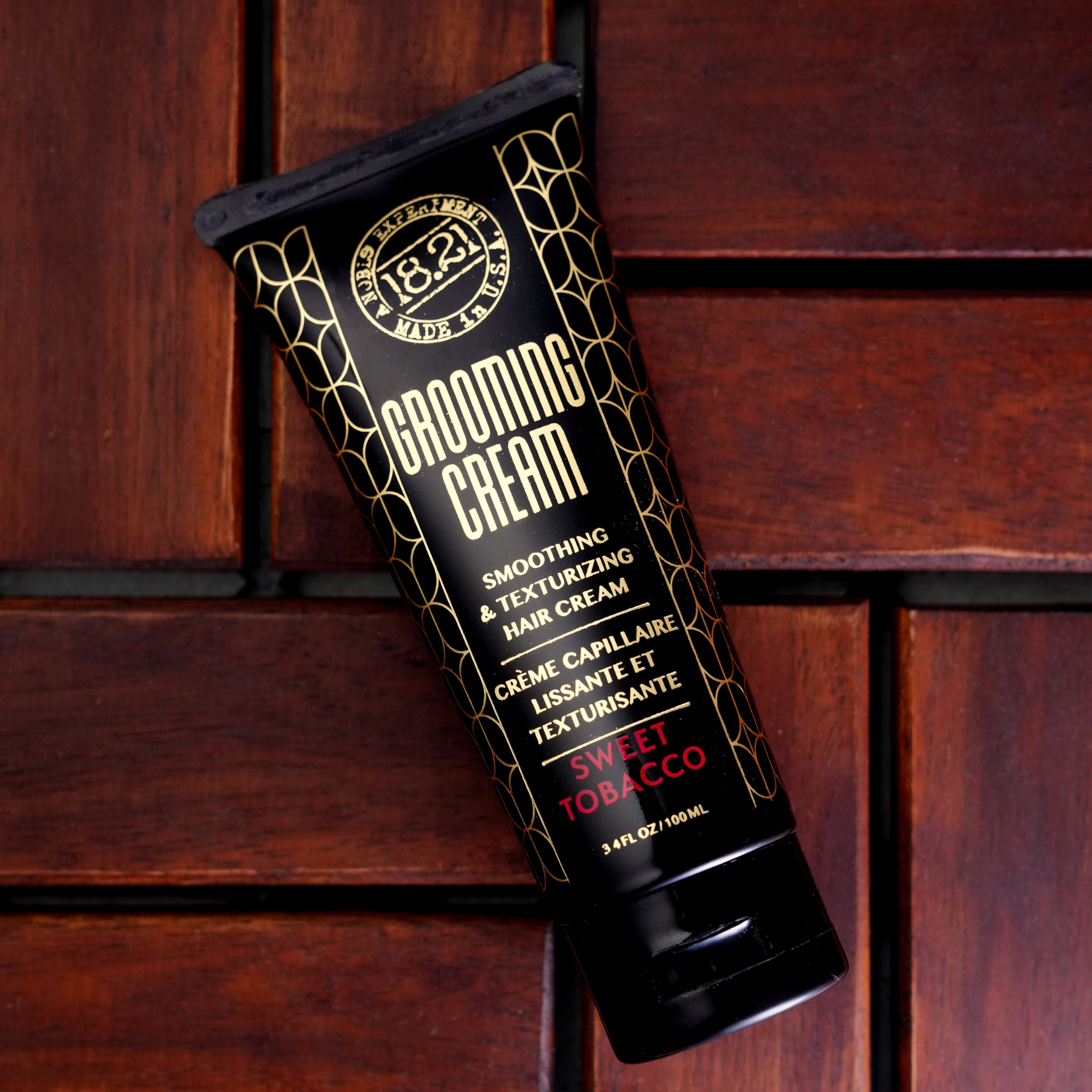 Black tube of grooming cream with gold and red text on a wooden background