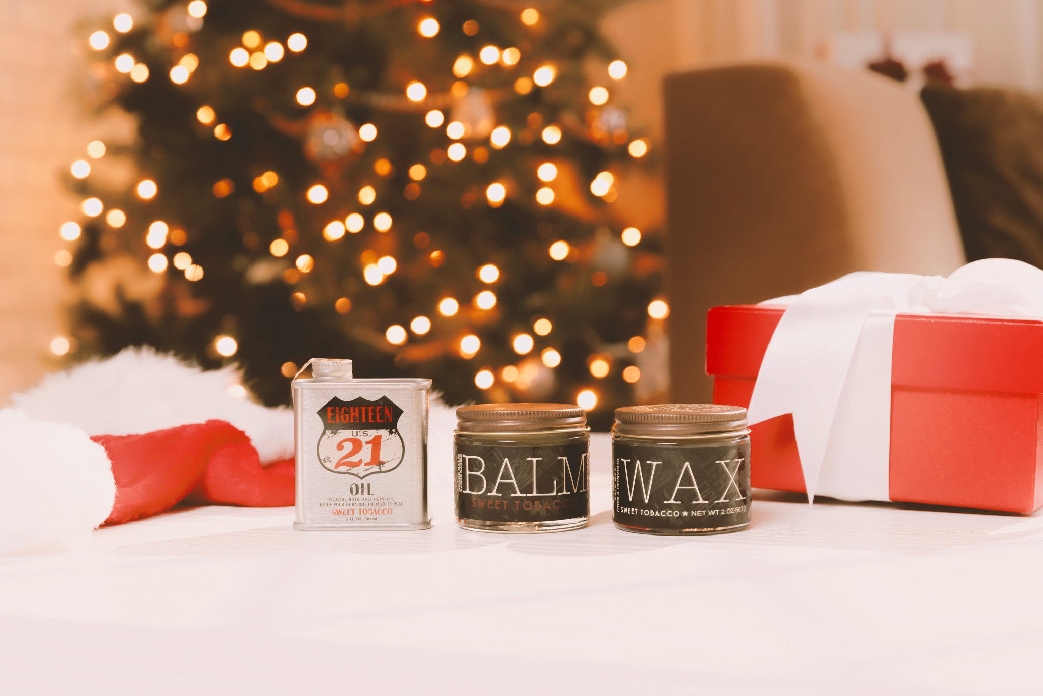 Three small containers labeled 'Balm', 'Wax', and '21' on a surface with a Christmas tree in the background.