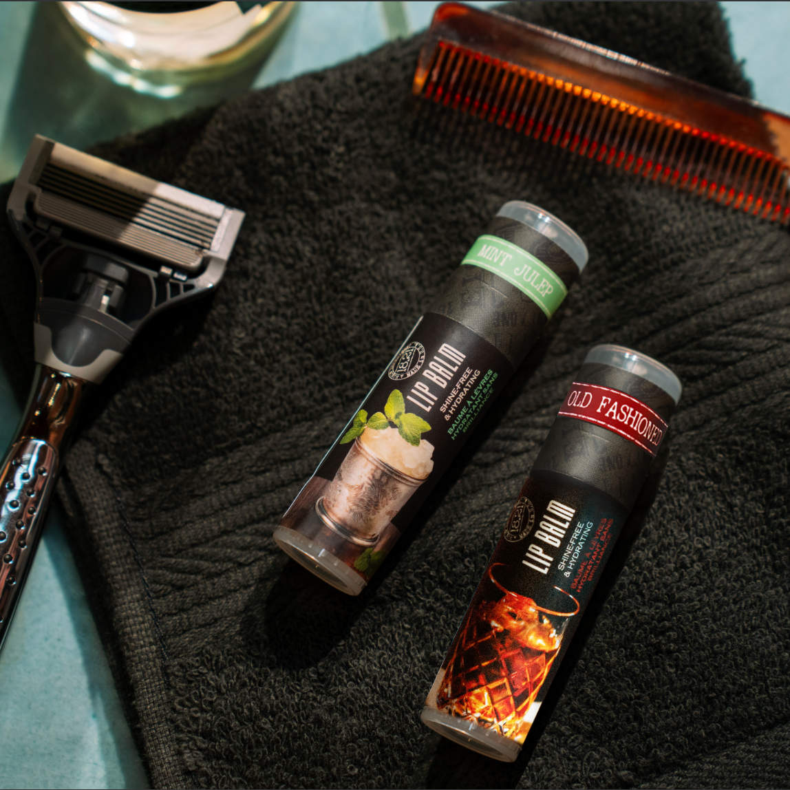 Shaving products including a razor, bottles, and a comb on a towel. With old fashioned and mint julep lip balm