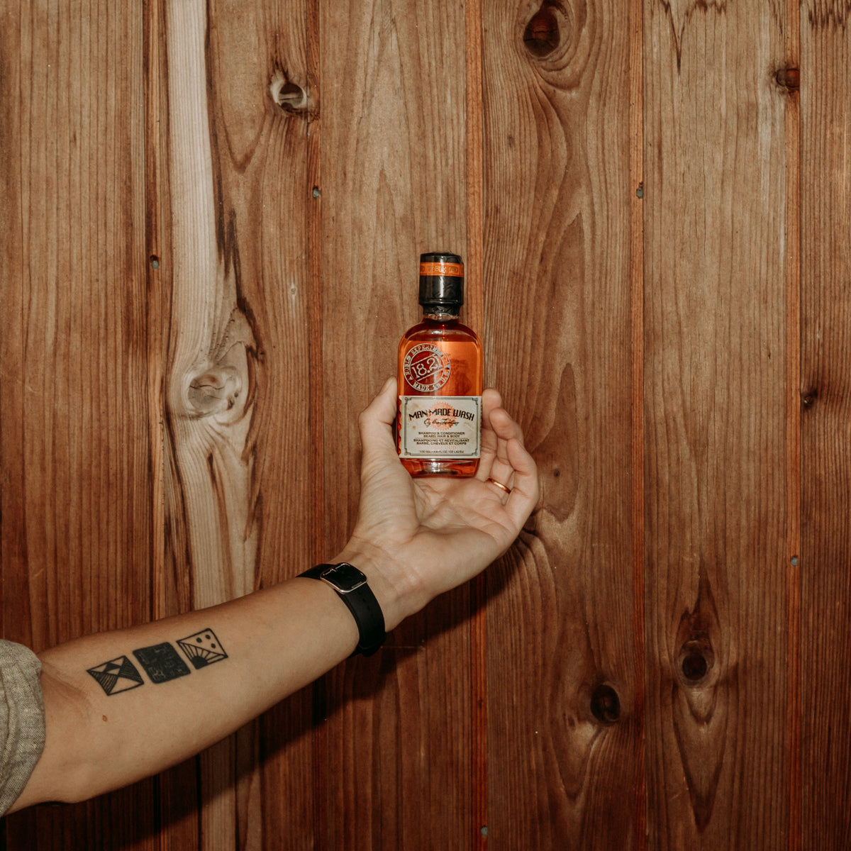 Hand holding a bottle of Man Made Wash in 3.4 oz travel size  against a wooden background