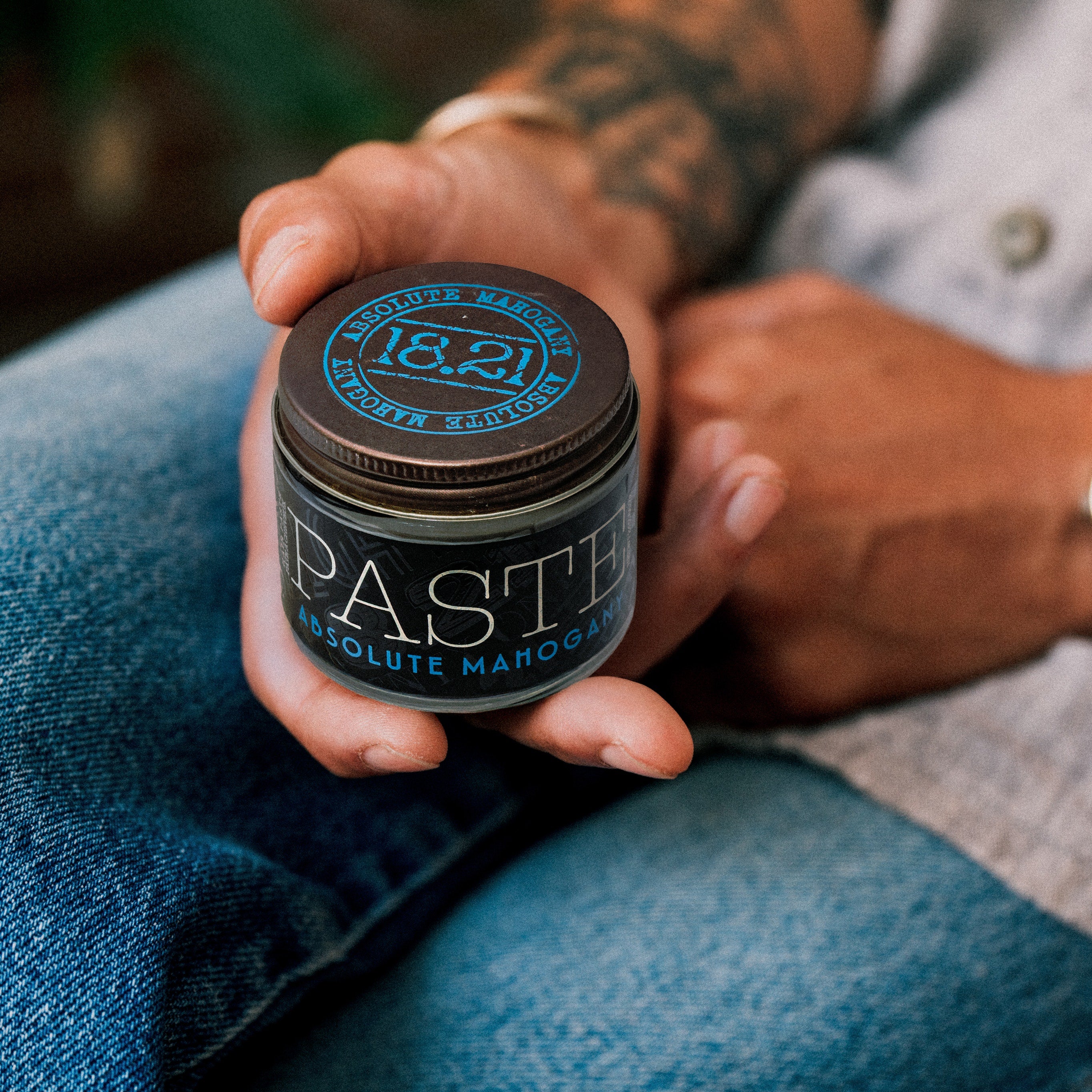 Hand holding a jar of 18.21 Paste Absolute Mahogany against a blurred background